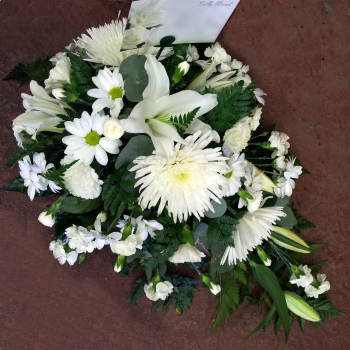 A teardrop-shaped floral arrangement with a mix of white flowers and green foliage, laying on a flat surface.