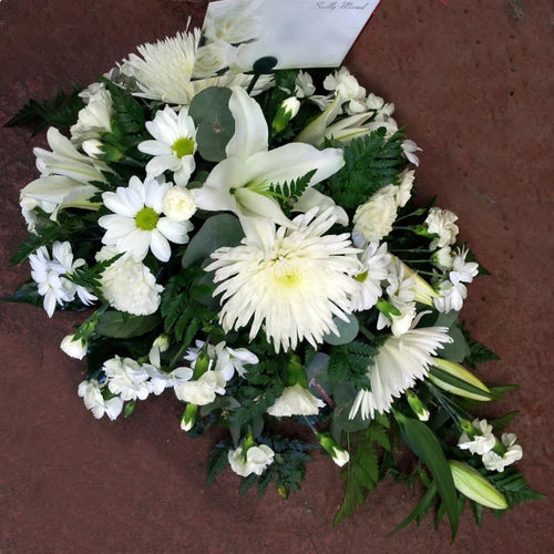 A teardrop-shaped floral arrangement with a mix of white flowers and green foliage, laying on a flat surface.
