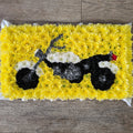 A flower arrangement shaped like a motorbike with  a yellow background