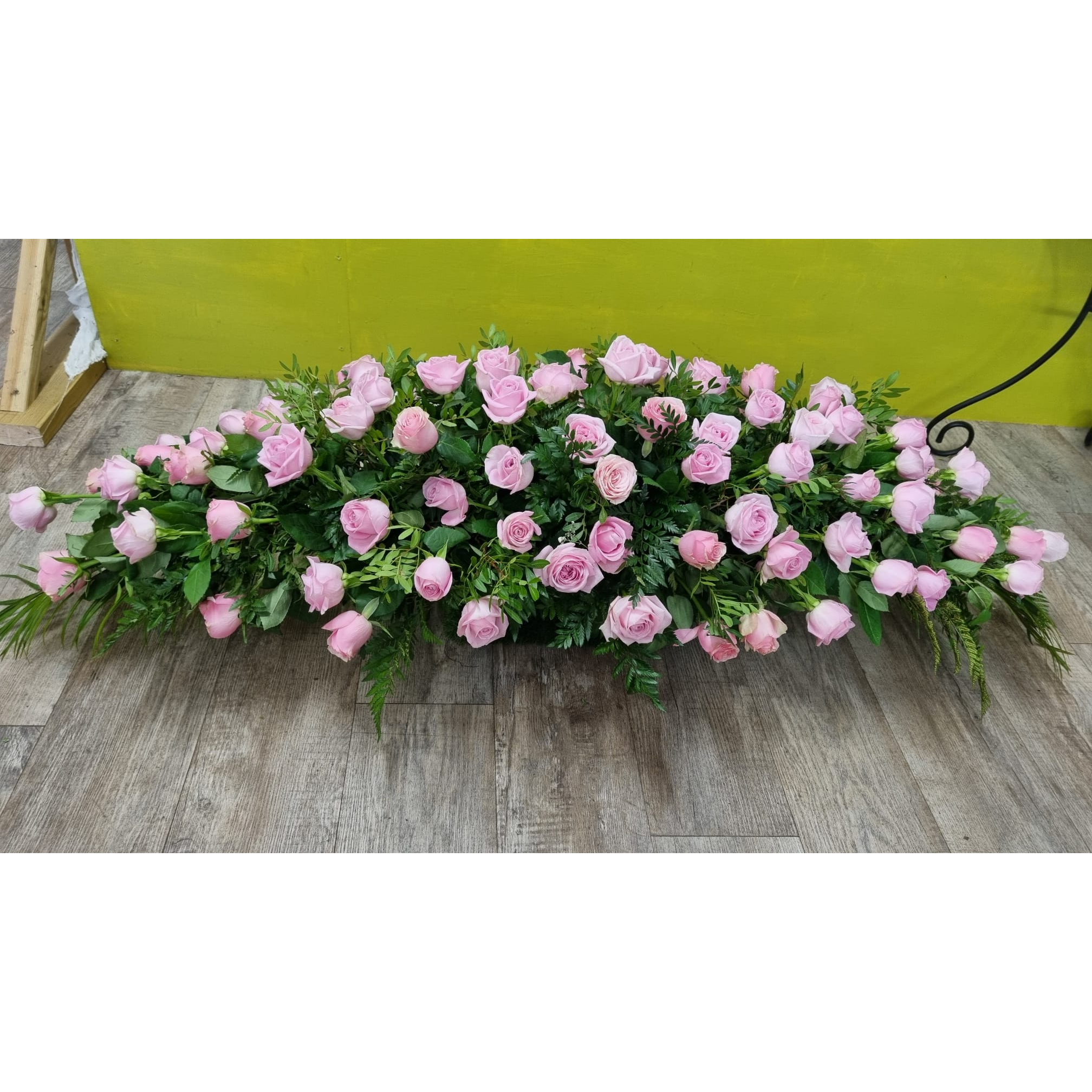 A large coffin spray arrangement with roses and dark green foliage.