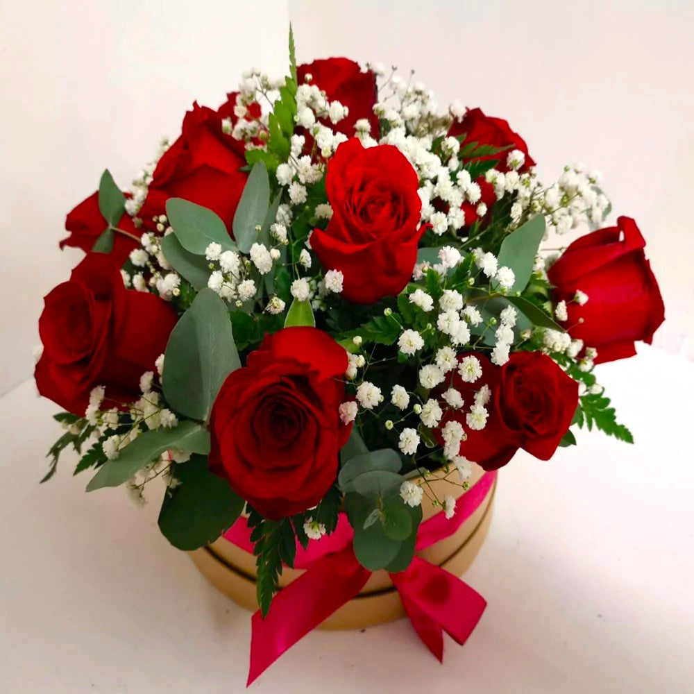 A hatbox arrangement of red roses, white gypsophilia, and green foliage.