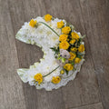 Crescent-shaped floral arrangement with yellow and white flowers and a small teddy bear in the center