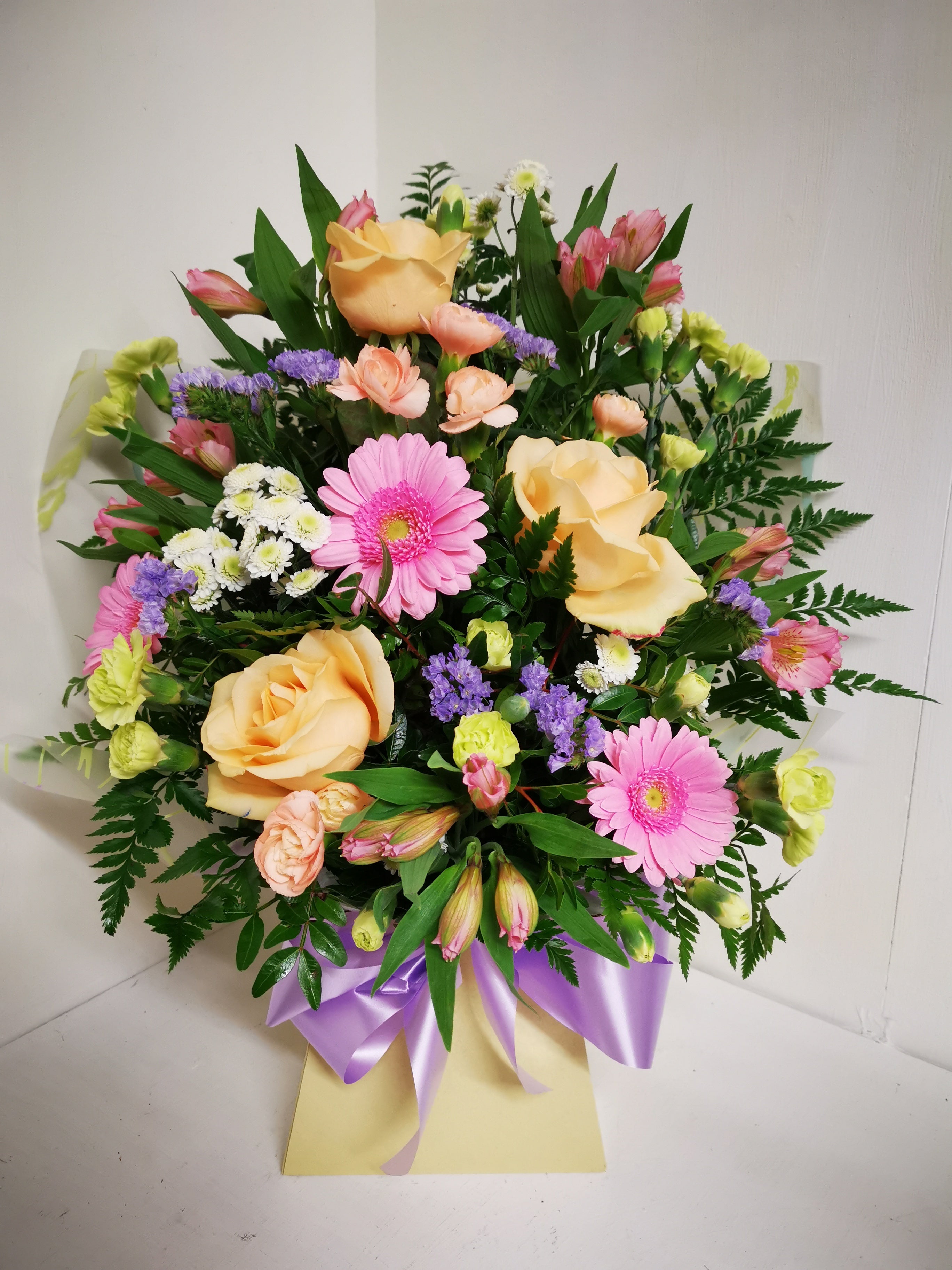 A colorful floral arrangement featuring roses, gerberas, alstromeria, spray carnations, statice, and chrysanthemums set in floral foam.