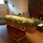 A wicker casket adorned with a fresh greenery garland