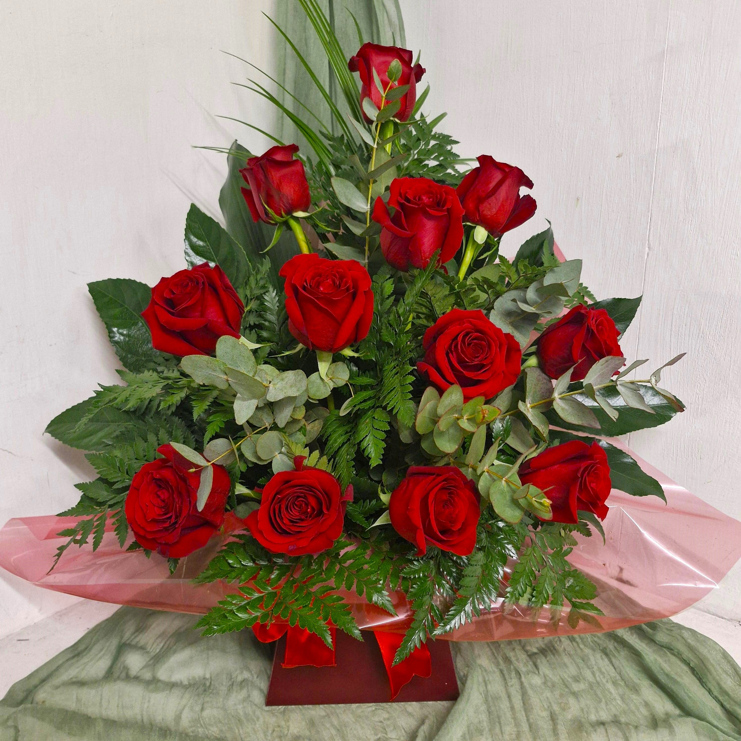 A floral arrangement featuring roses with mixed greenery, displayed in watered floral foam, presented in a box