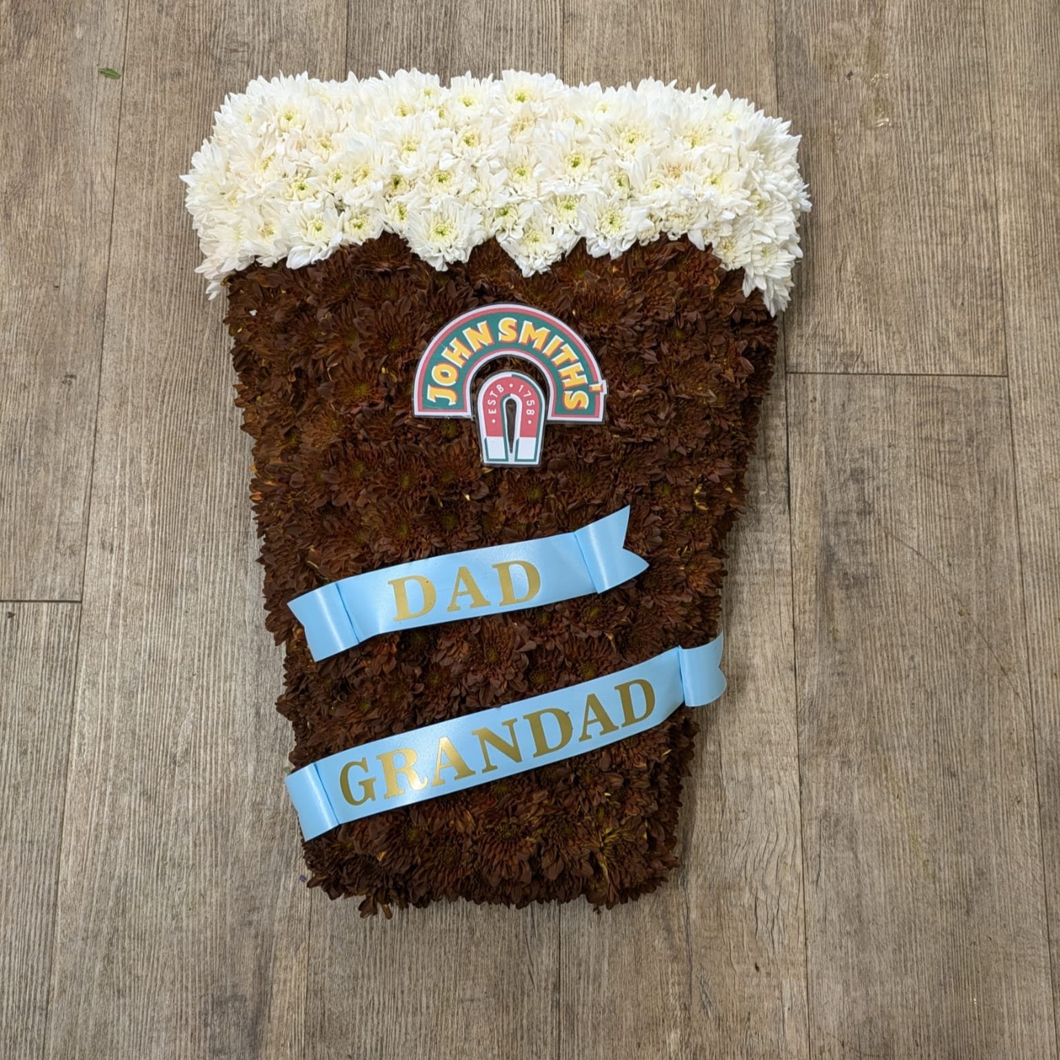 A decorative John Smith's pint glass made of flowers, with a label on top and personalized text 'Dad Grandad' on the front.