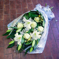 A bouquet of roses, lilies, and gypsophila with mixed greenery, wrapped in cellophane