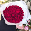 A large bouquet of deep red roses wrapped in white cellophane, held by a person