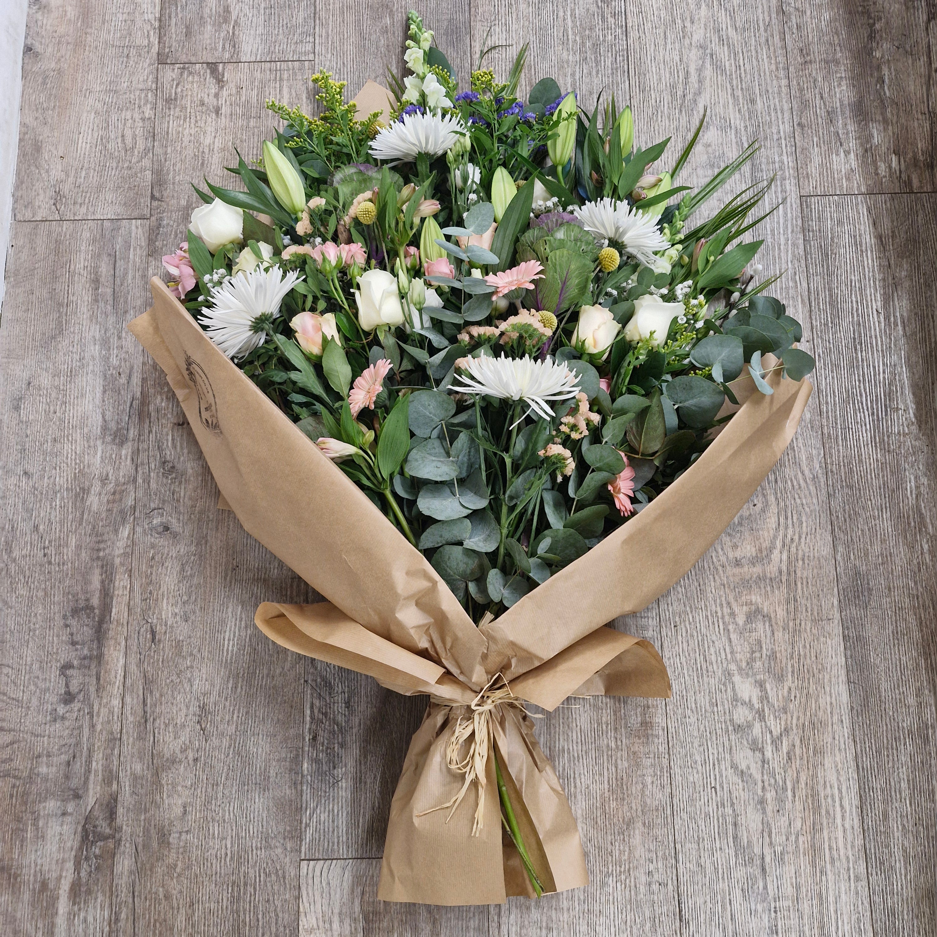 A bouquet of flowers arranged in brown paper and tied with raffia, featuring a variety of flowers.