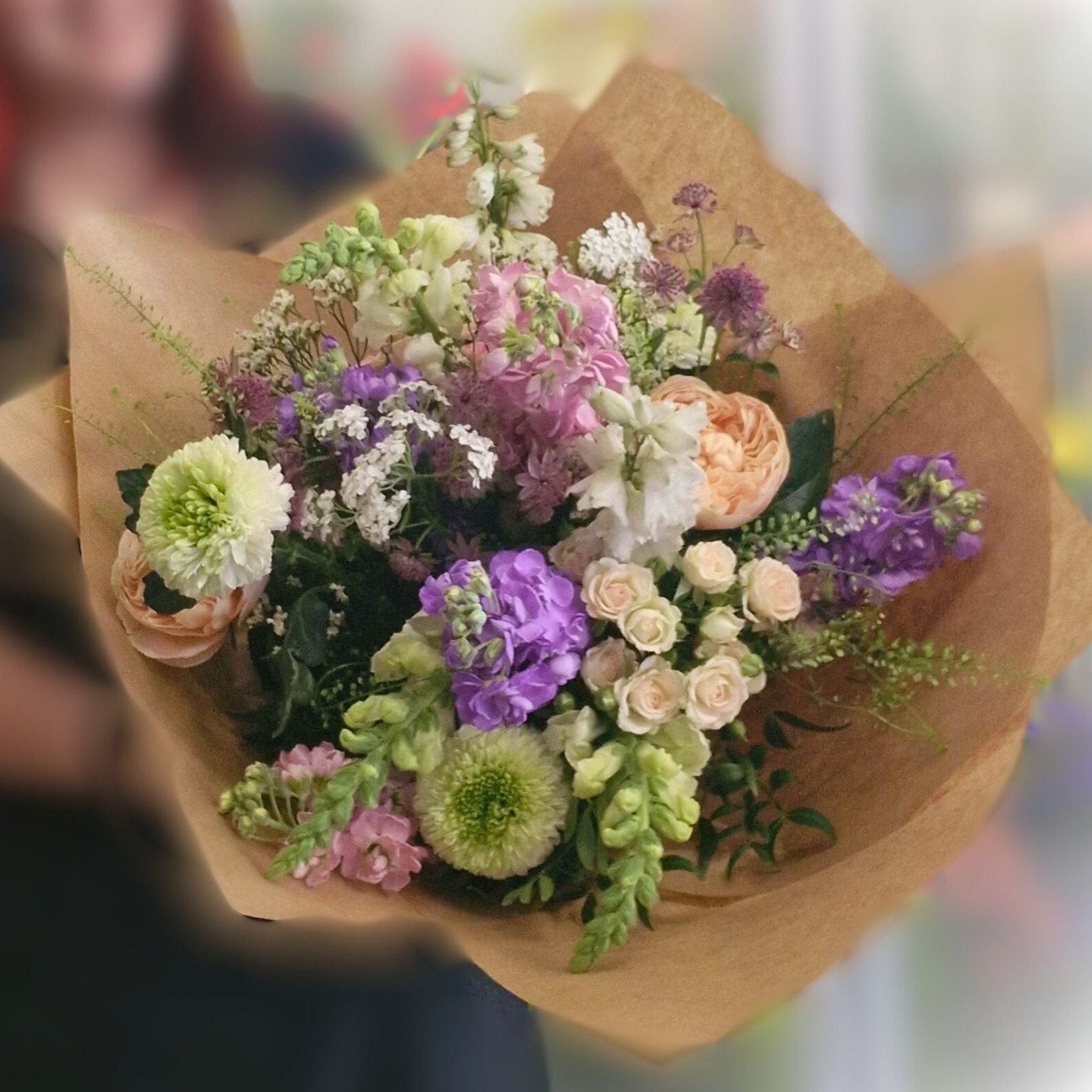 A handtied style bouquet with a mixture of flowers wrapped in natural brown paper and tied with raffia.