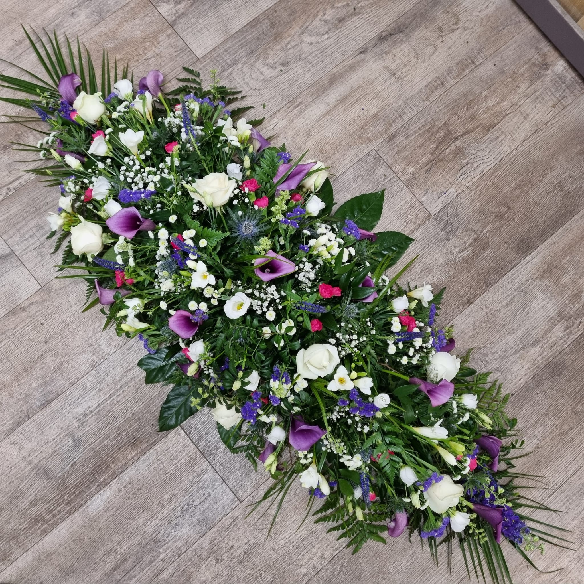 A floral arrangement of purple callas and white roses with green foliage, designed as a 4ft double-ended coffin spray.