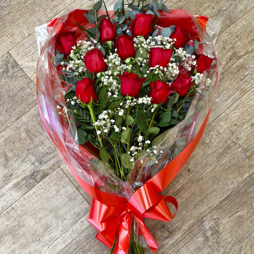 A rose bouquet consisting of large-headed roses with foliage and gypsophila, wrapped in cellophane and tied with a ribbon.