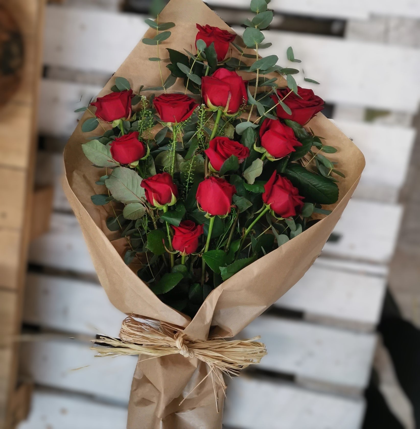 A bouquet of roses with greenery, wrapped in brown paper and tied with raffia