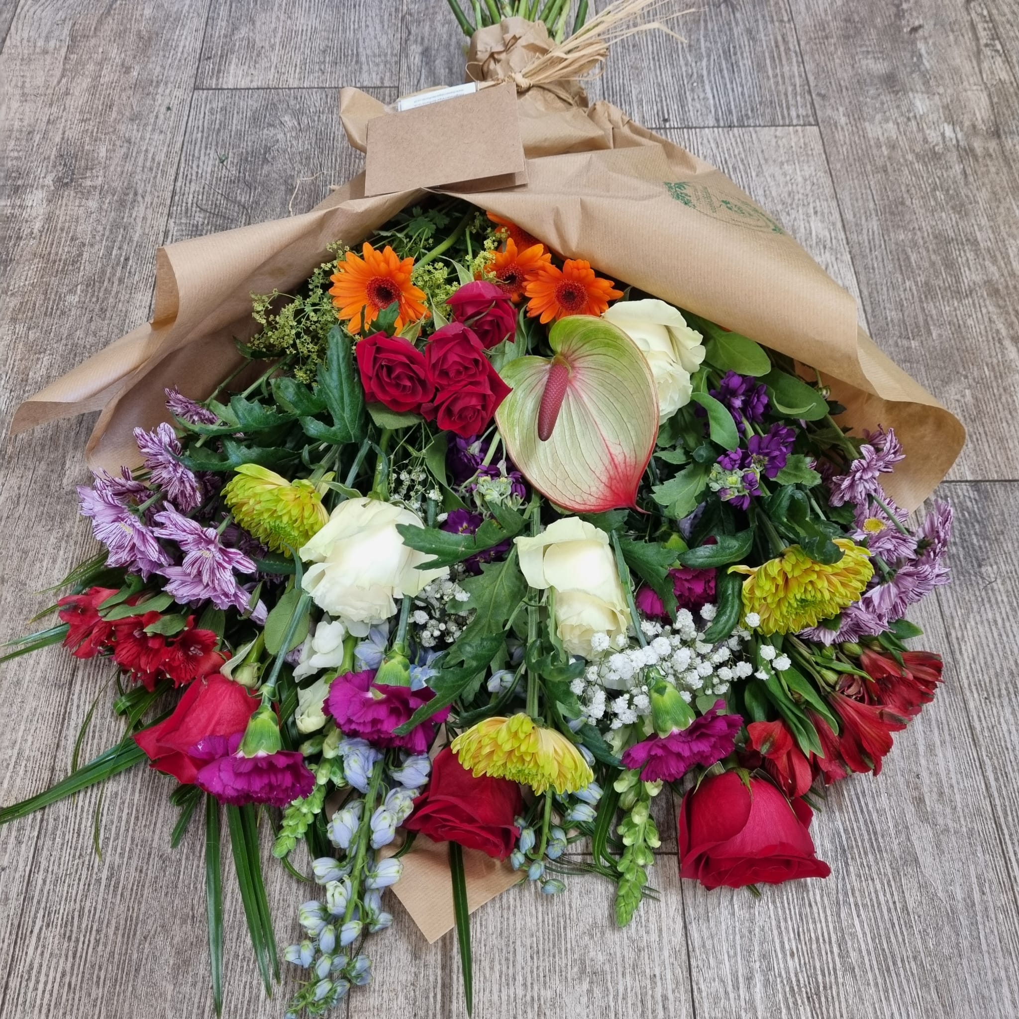 A vibrant bouquet of assorted flowers including red, white, and purple hues, wrapped in natural brown paper.