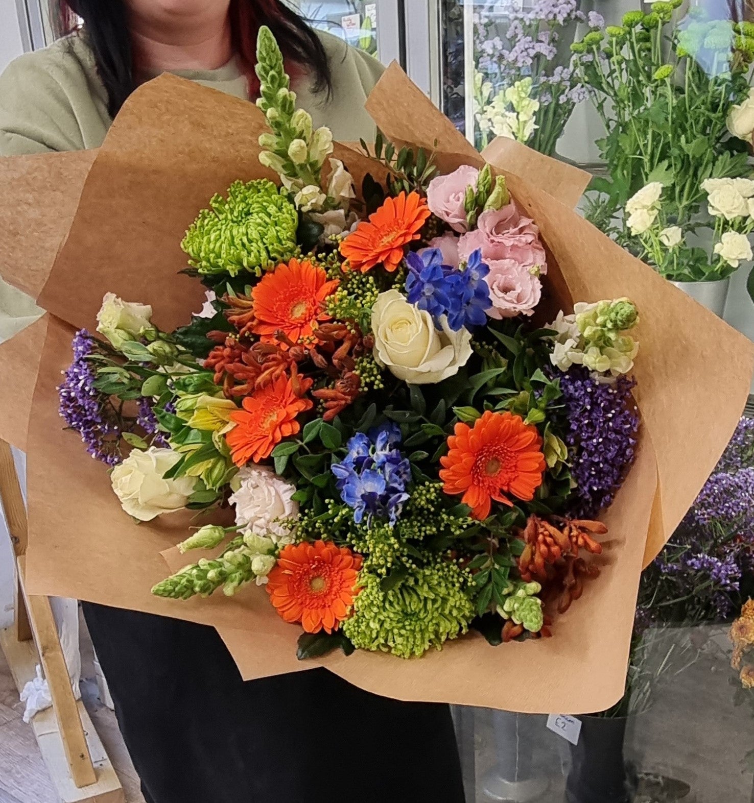 A hand-tied bouquet with a variety of colorful flowers including oranges, purples, and limes, wrapped in brown paper.