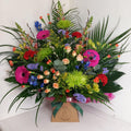 A vibrant floral arrangement featuring a variety of flowers such as spray roses, Germinis, Chrysanthemum blooms, Alstromeria, Delphinium, Carnations, Spray carnations, Antirrhinums, Statice, Solidago, and mixed greenery, presented in a box.