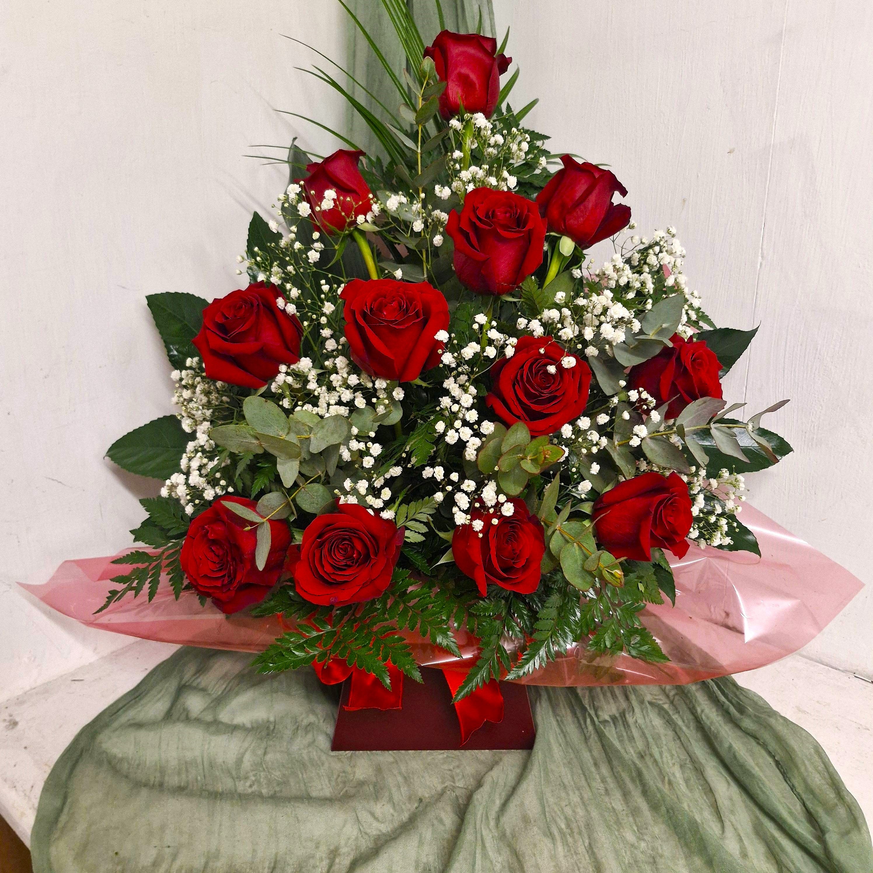 A floral arrangement featuring red roses with white Gypsophilia and mixed greenery, presented in a watered floral foam.