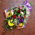 A traditional bouquet of flowers with a variety of colours, wrapped in cellophane and tied with a ribbon.