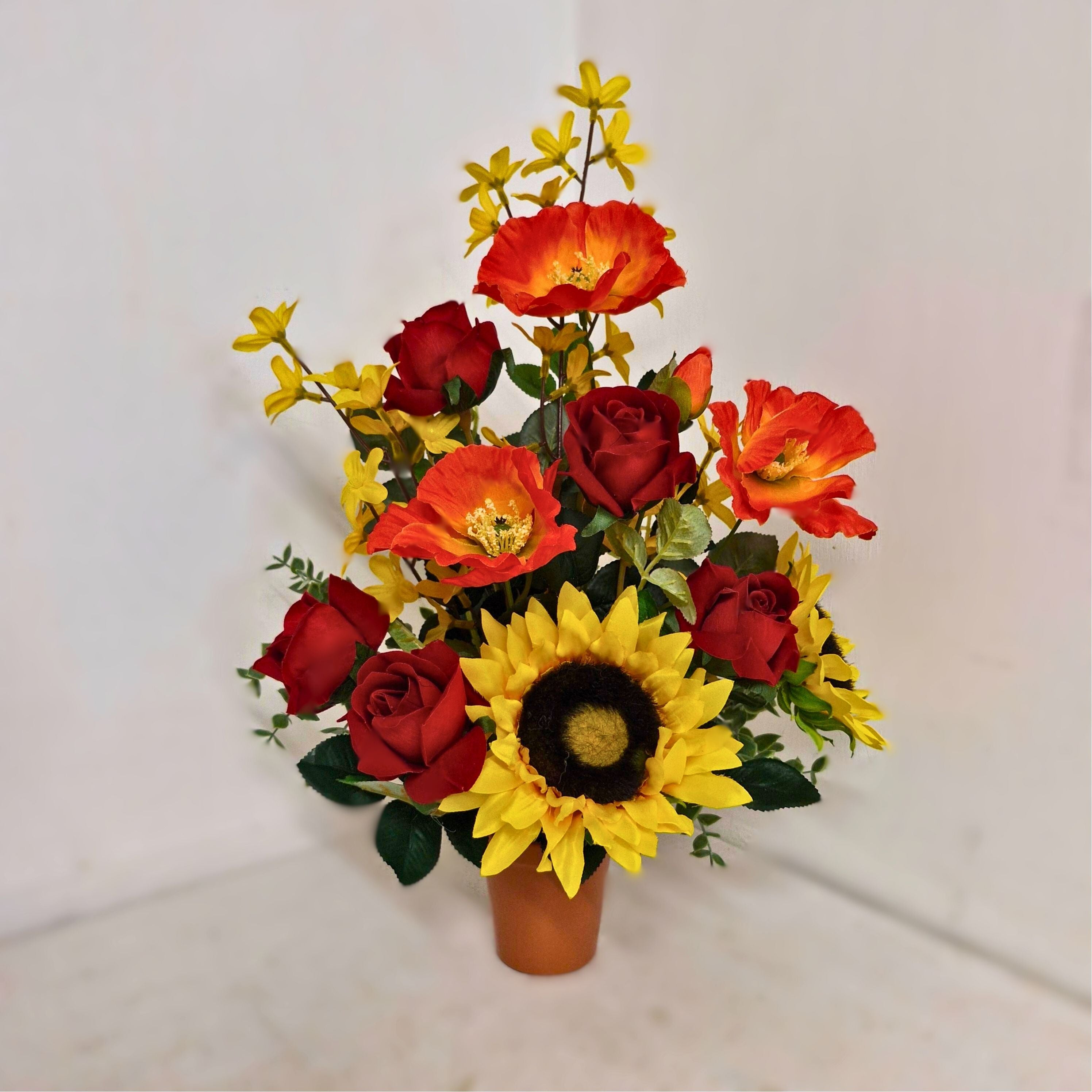 An upright cement pot with a bouquet of artificial flowers that include sunflowers, roses, and other colorful flowers.