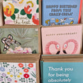 A variety of greeting cards with different designs, including some with floral patterns and animal illustrations, displayed in a card holder.