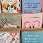 A variety of greeting cards with different designs, including some with floral patterns and animal illustrations, displayed in a card holder.
