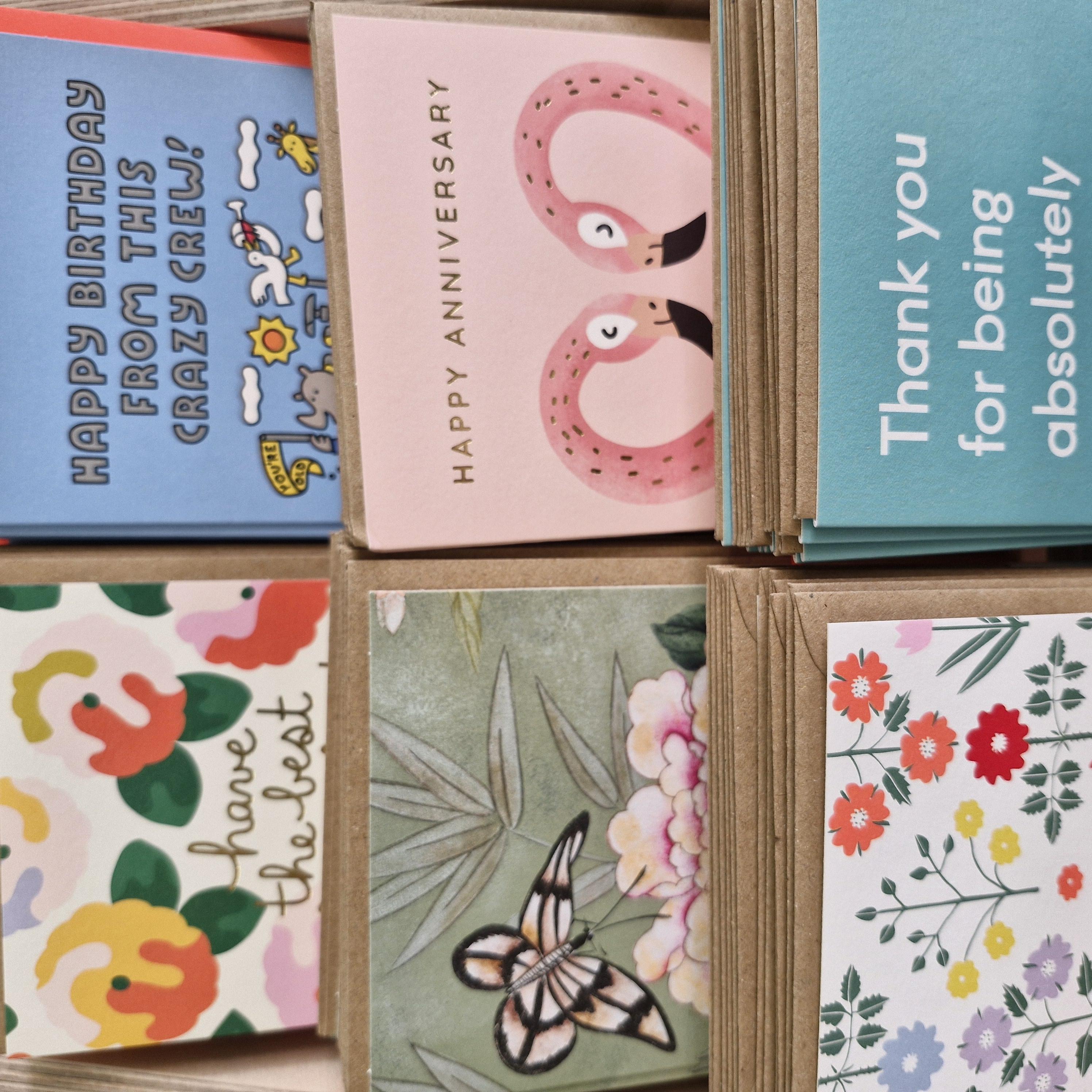 A variety of greeting cards with different designs, including some with floral patterns and animal illustrations, displayed in a card holder.