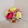 A round style artificial floral arrangement with a variety of flowers in pink, yellow, and white, set in a cement container.