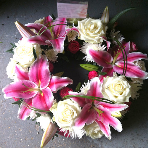 A wreath made up of pink lilies and roses, arranged in a circular form