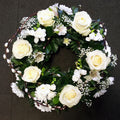 A floral wreath with white roses and green foliage arranged loosely.