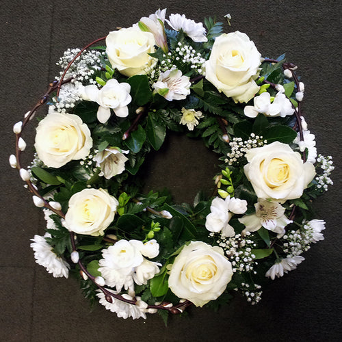 A floral wreath with white roses and green foliage arranged loosely.