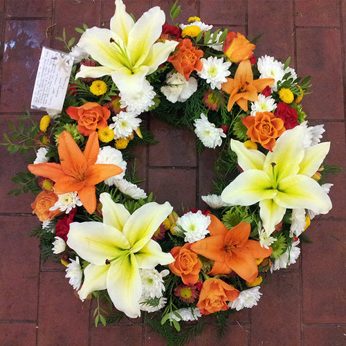 A 14 inch round wreath made up of orange, yellow, white and red flowers