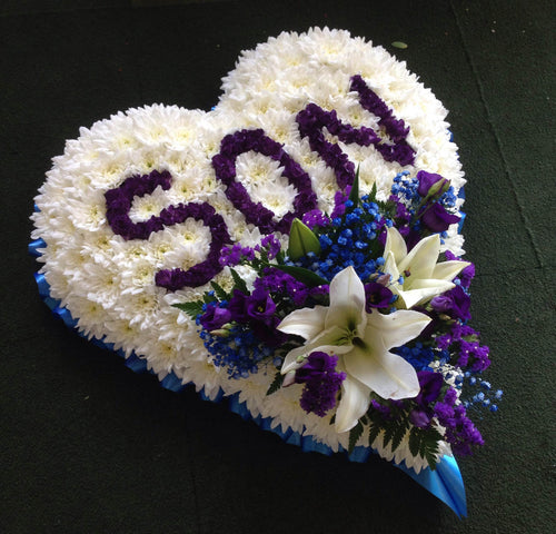 A heart-shaped floral arrangement with 'Son' written in purple on the top edge, with a spray of blue flowers and a white lily.