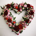 A heart-shaped floral wreath with a mix of red and pink flowers, including orchids and roses.