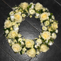 A classic cream rose wreath arrangement consisting of white roses and small greenery accents.