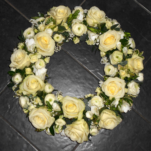 A classic cream rose wreath arrangement consisting of white roses and small greenery accents.