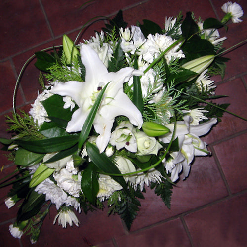 A double ended floral arrangement featuring white lilies and other white flowers with green foliage