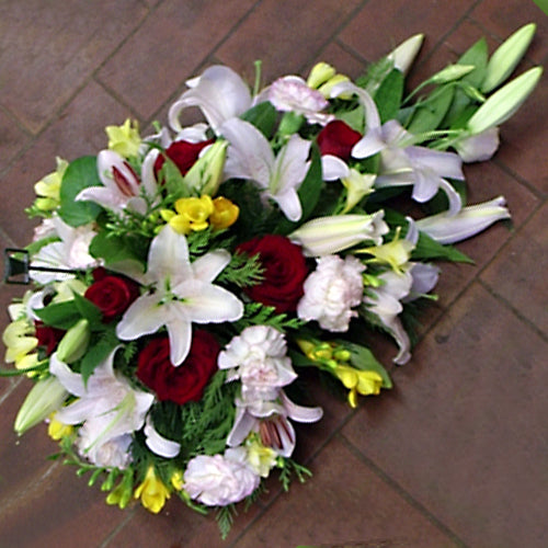 A floral arrangement featuring lilies and roses in a teardrop shape