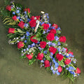 A large, diamond-shaped floral arrangement featuring red roses and blue delphinium