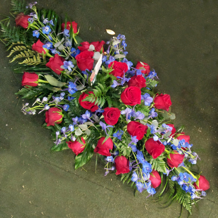 A large, diamond-shaped floral arrangement featuring red roses and blue delphinium