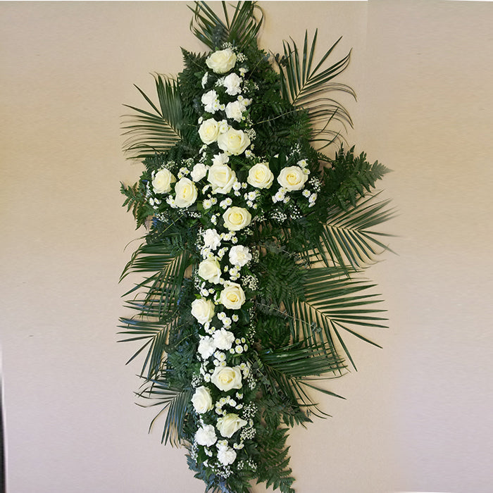 A floral arrangement featuring a white cross with large white avalanche roses and greenery