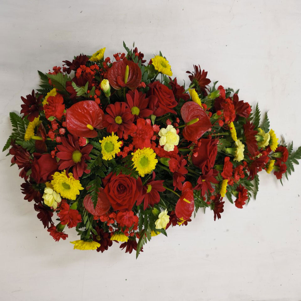 A floral arrangement featuring deep red flowers, with yellow and lemon accents, shaped in a teardrop form.