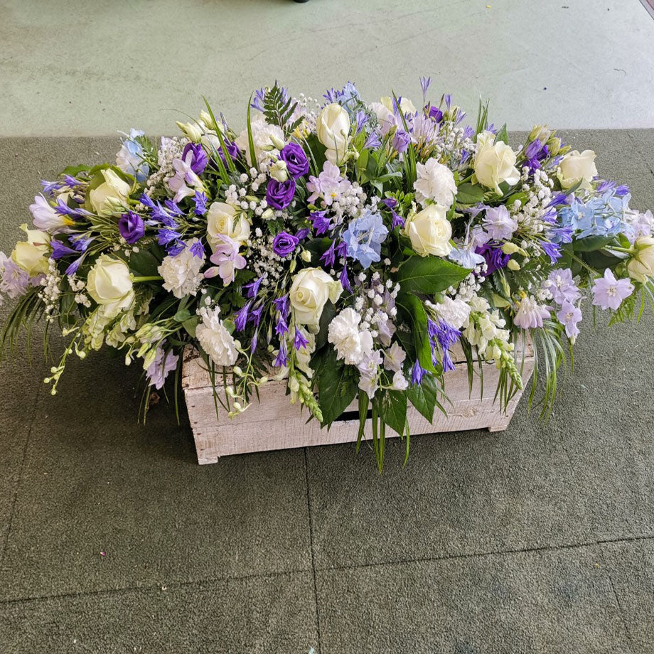 A floral arrangement featuring a mix of blue, lilac and white flowers and green foliage