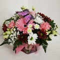 A floral arrangement featuring pink, white, and burgundy flowers with a decorative butterfly on top.