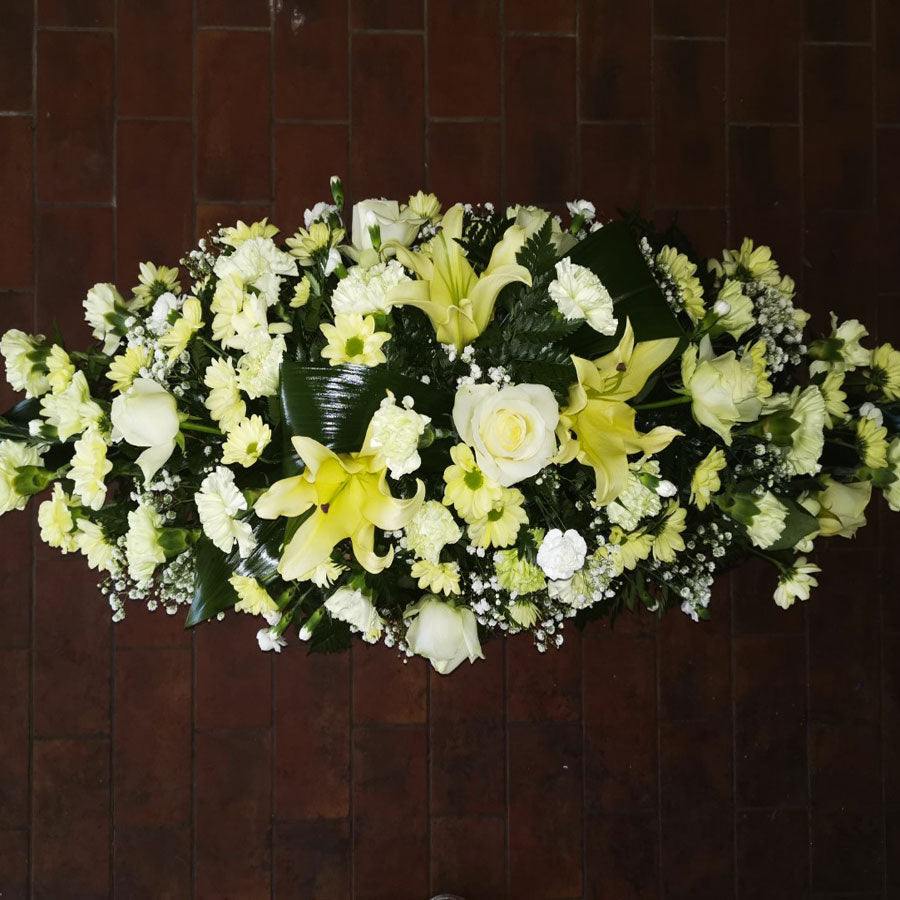 A traditional casket spray with cream and white flowers