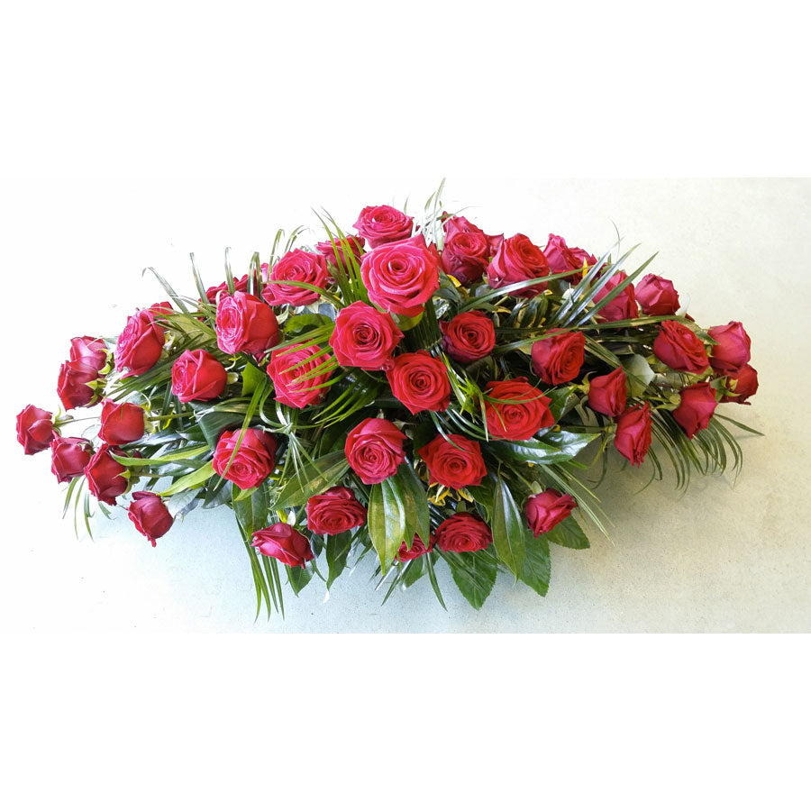 A floral casket spray with red roses and green leaves