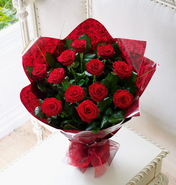 A handtie of large headed roses arranged with glossy foliage, wrapped in cellophane with a bow.