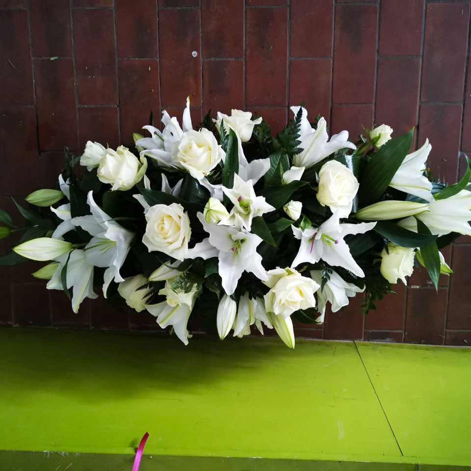 A traditional casket spray with roses and lilies, arranged in a double ended spray