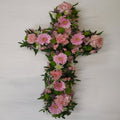 A decorative pink floral cross with green leaves