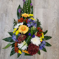 A floral tribute in a teardrop shape, featuring a variety of flowers, including yellow, orange, and blue, complemented by green foliage.