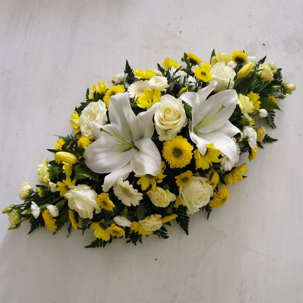 A floral arrangement featuring yellow and white flowers, including lilies, arranged in a double ended spray